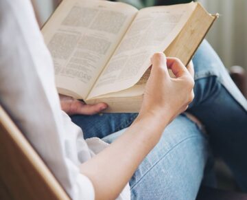 Young lady's hands are holding big book while reading it