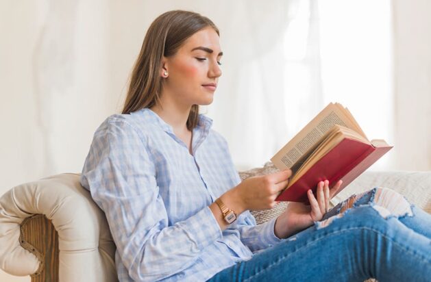 woman is holding a book while reading it on the sofa